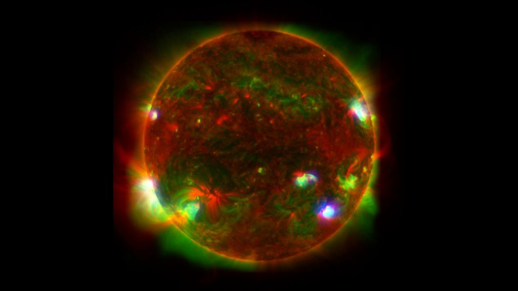 Le lunghezze d'onda della luce provenienti da tre osservatori spaziali sono sovrapposte per fornire una visione unica del Sole nell'immagine a sinistra. La luce a raggi X ad alta energia rilevata da uno di quegli osservatori, il NuSTAR della NASA, è vista isolata a destra; è stata aggiunta una griglia per indicare la superficie del Sole
